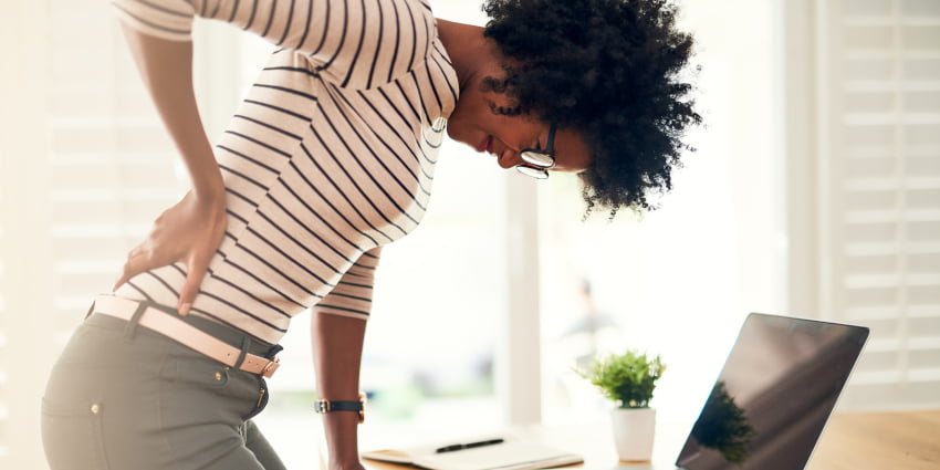 A young woman holding her sore back while getting up from her desk at home