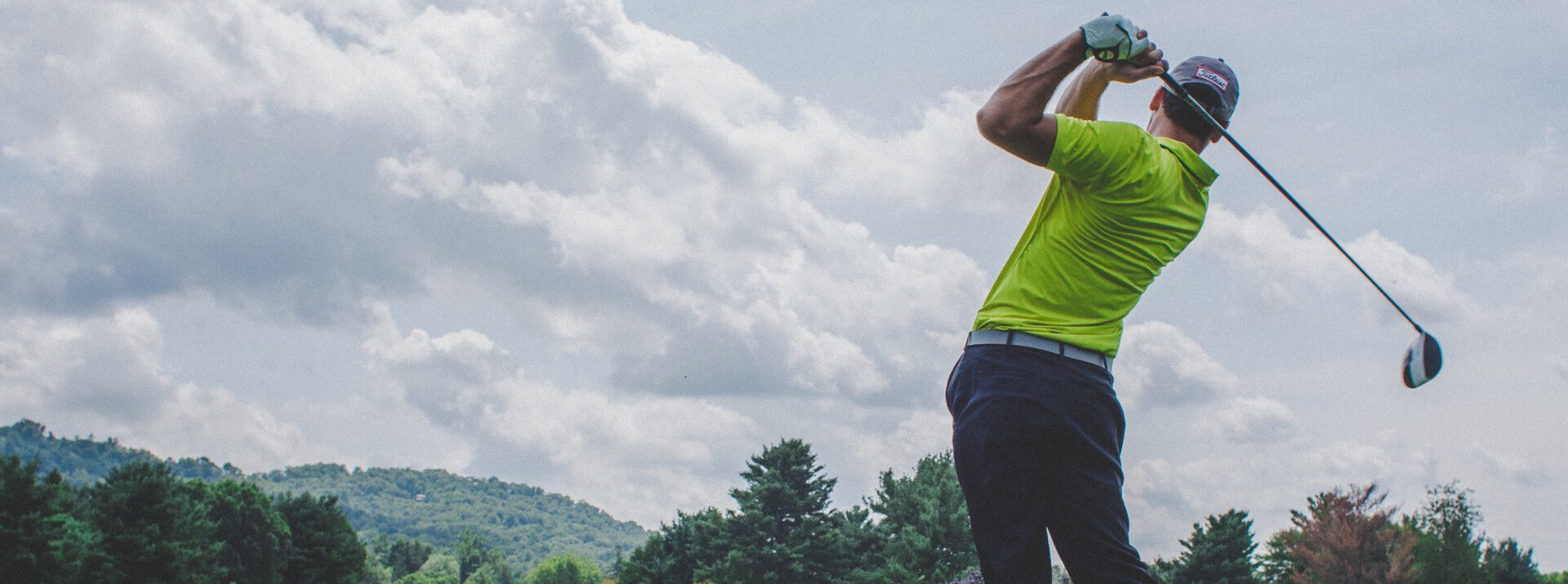 A man swings a golf club and looks down the fairway
