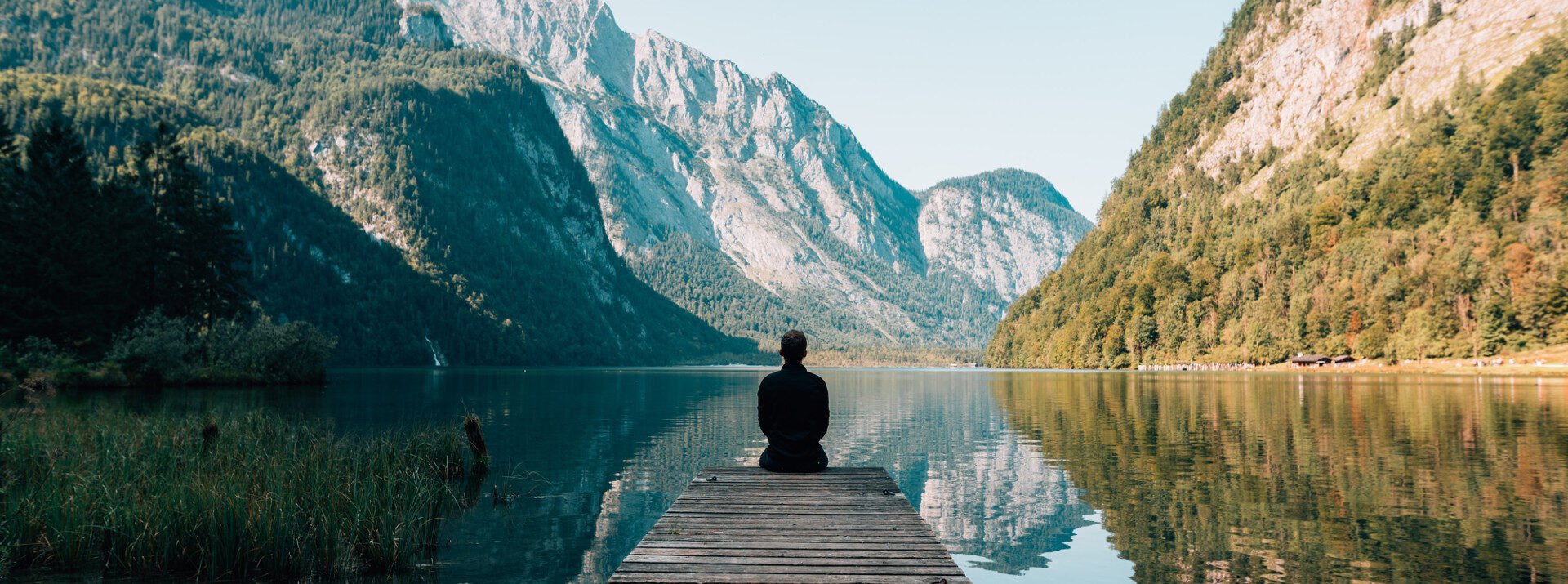 Woman sitting on a dock at a lake surrounded by mountains