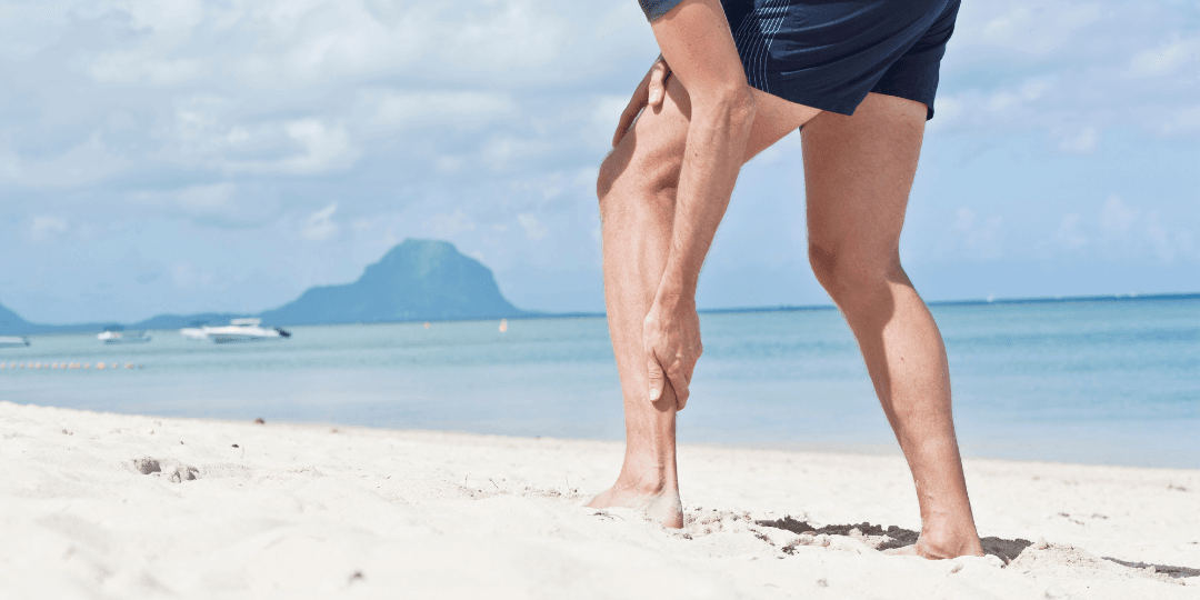 Man walking on beach grabbing injured Achilles tendon